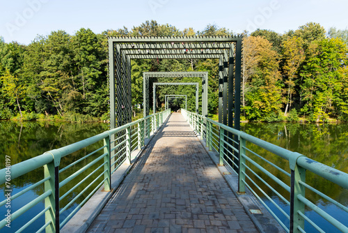 Pedestrian bridge over the river against the background of the river and trees and reflection in the water.