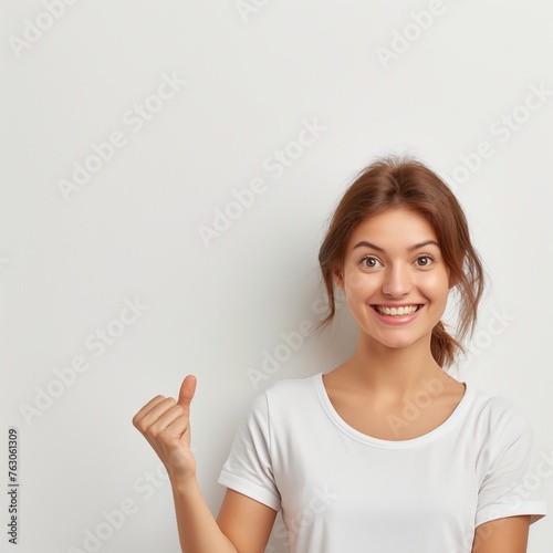 A smiling young woman gestures with her thumb to an empty space, ideal for advertising.