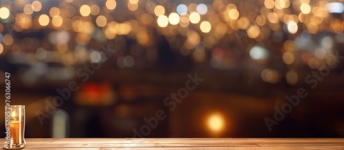 An ambertinted glass of beer rests on a rustic wooden table in the city during an evening event. The font of the sky is dark as night, illuminated by automotive lighting and the silhouette of a tree photo