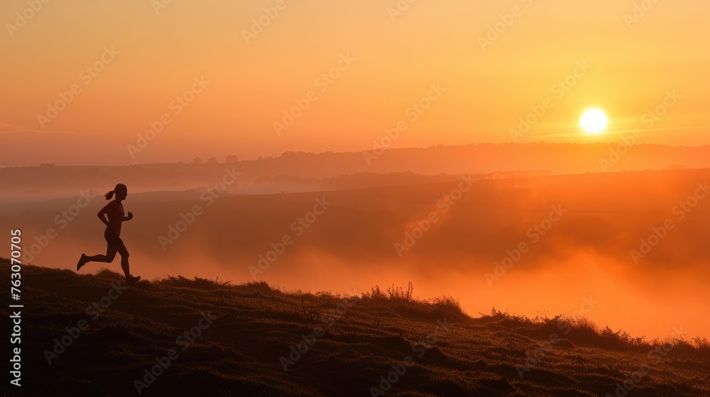 Silhouette of a runner on a misty hillside at sunrise with a warm orange sky