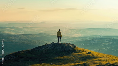Lone adventurer stands on a mountain peak at sunset, overlooking a vast landscape