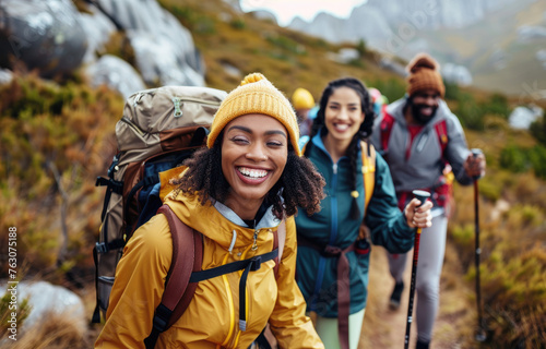 Happy group of friends hiking and smiling while holding walking sticks on mountain path