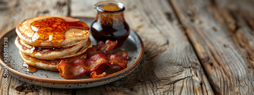 Buckwheat pancakes with a side of crispy bacon and a small jug of maple syrup on modern plate.