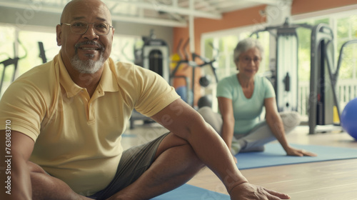 Two people are stretching on yoga mats in a gym with exercise balls in the background.