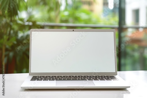 An open laptop with a blank screen on a white desk against a vibrant green background, perfect for remote work. Laptop on Office Desk with Greenery Backdrop