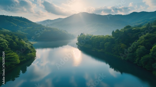 Serene sunrise over a tranquil mountain lake with reflections of hills and forest in the water.