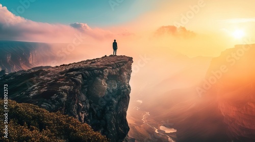 Person on cliff edge during a breathtaking sunrise with misty valleys below.