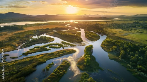Aerial view of a meandering river at sunset with golden light reflecting on water, surrounded by lush greenery and distant mountains.