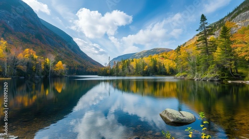 Serene autumn landscape with a reflective lake, surrounded by colorful fall foliage and mountains under a clear blue sky.