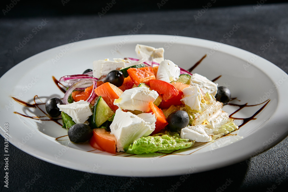 Greek salad closeup with feta cheese, Kalamata olives, and balsamic glaze on a white plate