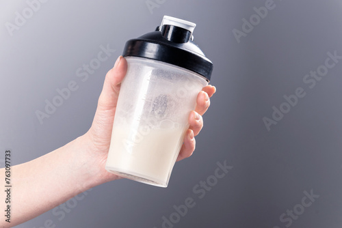 A female hand holds a mixer glass with collagen on a gray background. photo