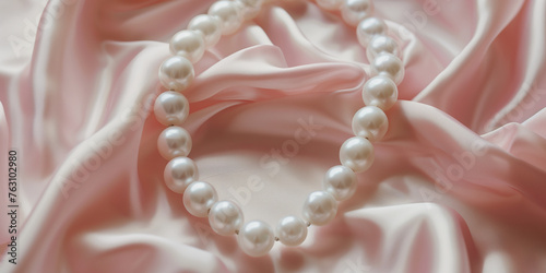White pearls bracelet on light pink satin cloth. Elegant wedding jewellery.