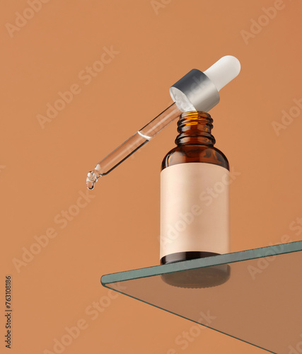 dropper bottle with clear liquid is placed on a glass shelf. The orange background contrasts with the bottle and dropper. A drop of liquid is visible at the tip of the dropper