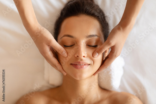 Masseuse hands massaging relaxed woman face, top view shot