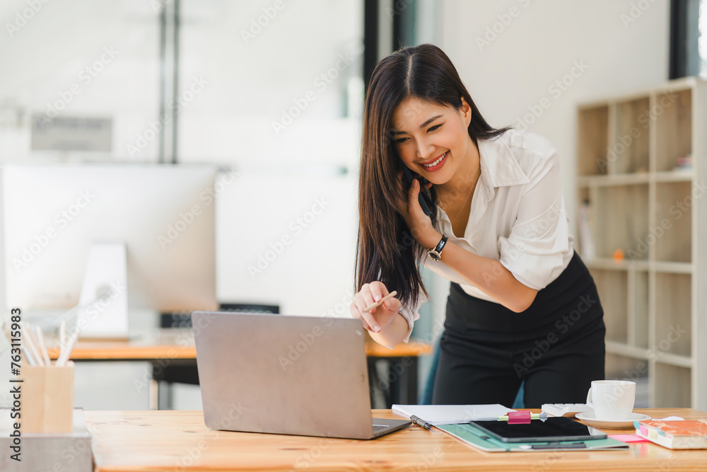 Busy professional businesswoman engages in a phone conversation while using laptop in a contemporary office workspace. Busy professional businesswoman engages in a phone conversation while using laptop in a contemporary office workspace.