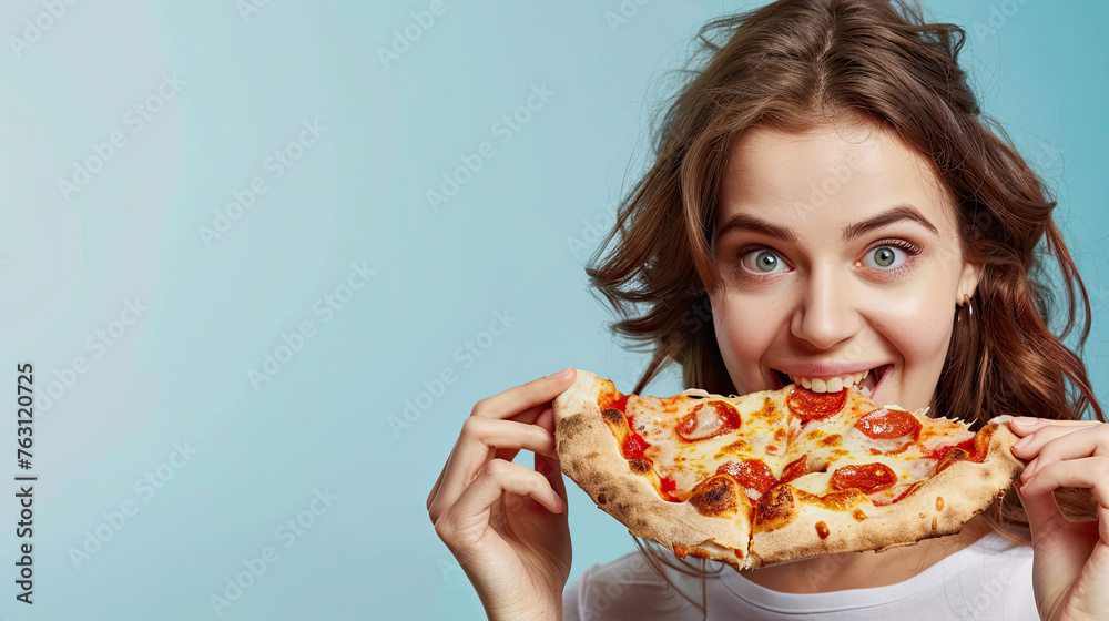 Attractive cheerful woman eats delicious Italian pizza, surprised with wonderful taste, on pastel blue background