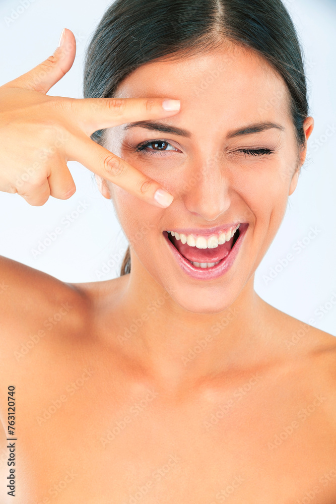 Obraz premium Peace hands, skincare and portrait of happy woman with wink in studio for wellness on white background. V, eyes and female model smile for dermatology, shine or natural cosmetic, treatment or results