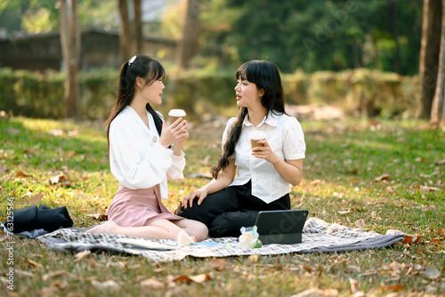 Fototapeta Naklejka Na Ścianę i Meble -  Carefree Asian women friends talking and enjoying coffee in the park after work