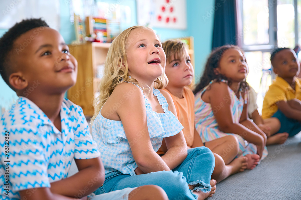 Obraz premium Line Of Smiling Primary Or Elementary School Students Sitting On Floor During Classroom Lesson
