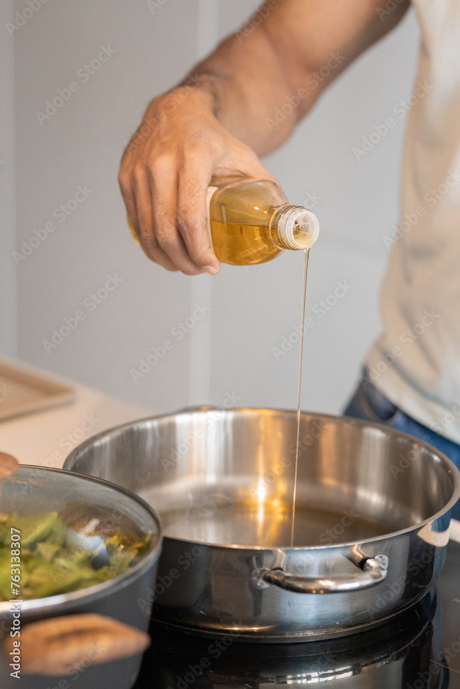 Black male hand pouring oil in a pot to cook a meat with vegetables, close up view