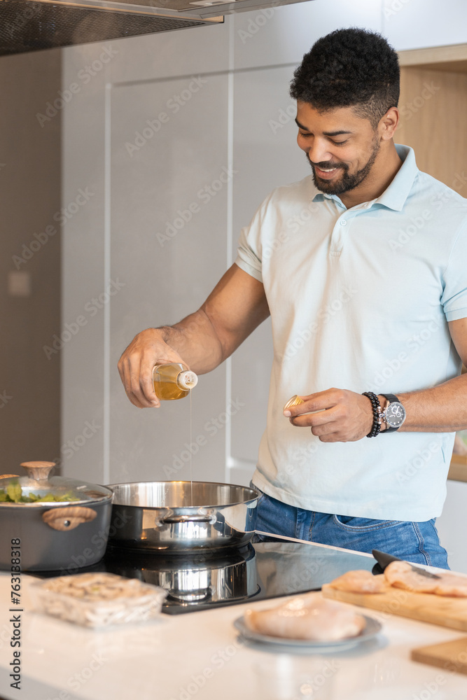 Handsome black man pouring oil in a pot to cook a meat with vegetables