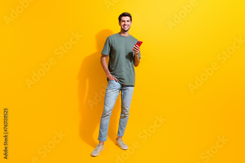 Full length photo of positive man dressed khaki t-shirt chatting instagram twitter telegram facebook isolated yellow color background