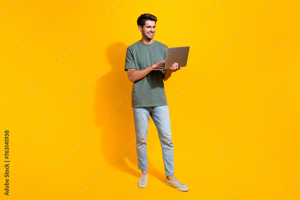 Full length photo of confident positive man dressed khaki t-shirt chatting twitter telegram facebook isolated yellow color background