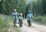 Three happy children ridding bicycles at country dirt road in woods.
