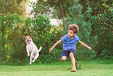 Boy playing with a paper plane at a backyard lawn and a dog jumping to steal the toy