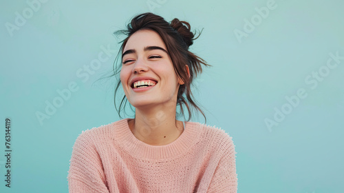 Young woman laughing at a good joke on pastel blue background