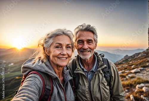 Old hiking couple enjoy the beautiful sunset in the mountain during a hiking tour and making a happy smiling self portrait selfie
