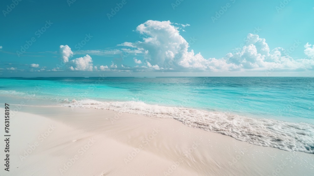 A tranquil stretch of white sandy beach meets the gentle waves of an azure sea under a bright blue sky dotted with fluffy white clouds