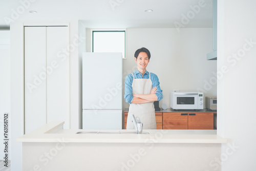 キッチンに立つエプロン姿の男性 © HML