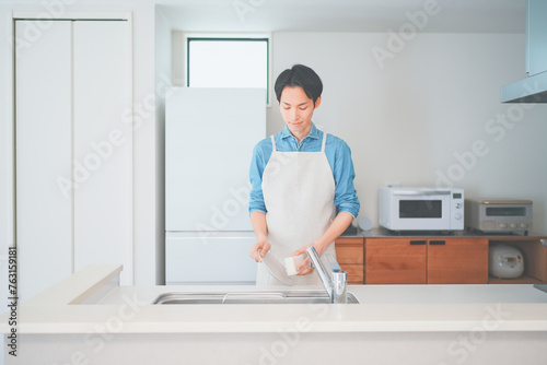 キッチンで皿洗いをするエプロン姿の男性