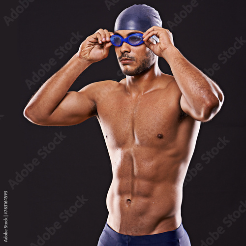 Studio, swimmer and man ready for competition, sport and training with exercise for body. Athlete, adult and male person with strength, professional and champion with goggles in black background
