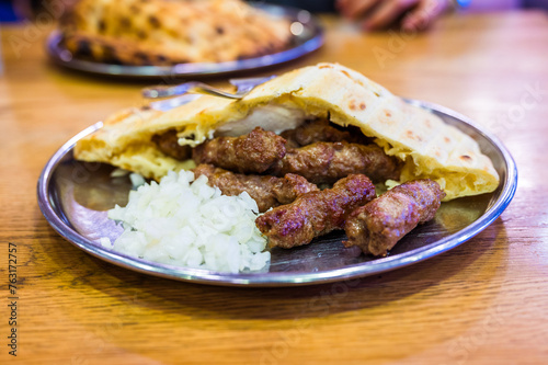 Traditional bosnian barbecue dish cevapi served with somun and chopped onions. Famous balkan BBQ dish served on an inox plate in Bascarsija, Sarajevo, Bosnia and Herzegovina.
