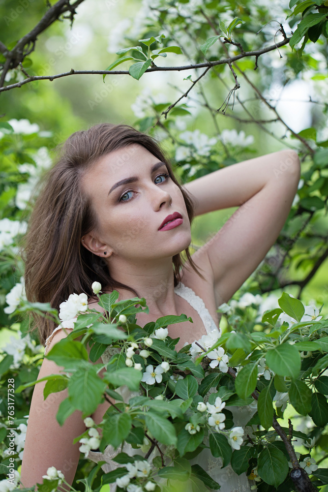 Perfect young adult brunette female model with fresh clean skin, bob haircut and natural makeup against green blurred leaves background with white spring flower Perfect young adult brunette female model with fresh clean skin, bob haircut and natural makeup against green blurred leaves background with white spring flower