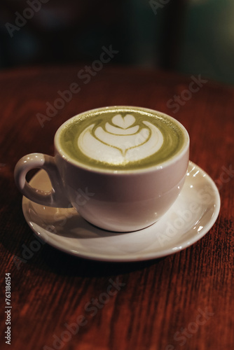 A cup with green Japanese matcha tea and milk foam on a wooden table
