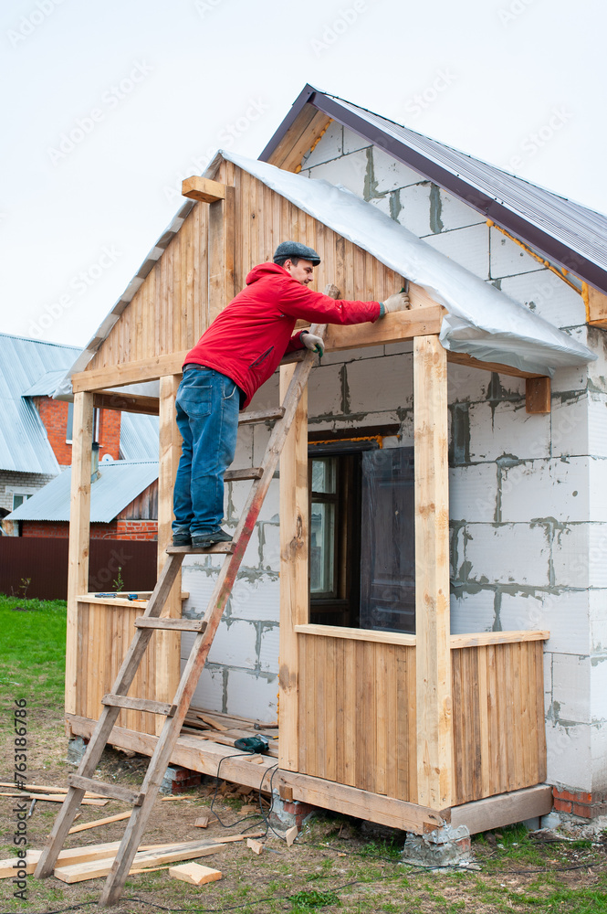 A worker builds a roof in a house while standing on a wooden ladder