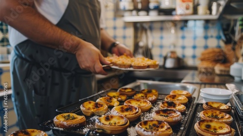 A pastry chef adds the finishing touches to freshly baked custard tarts in a well-equipped bakery with a blue-tiled backdrop.
