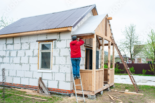 A worker builds a roof in a house while standing on a wooden ladder © Kiryakova Anna