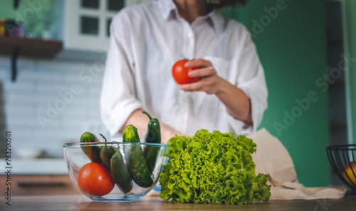 Woman in the kitchen puts vegetables and lettuce leaves in a glass bowl, healthy eating