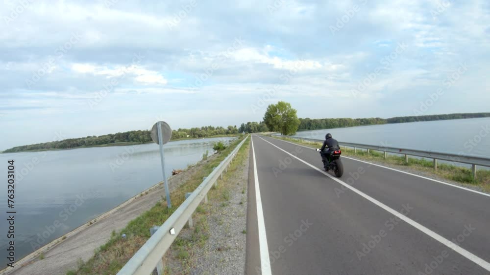 Biker riding on modern sport motorbike through road near lake. Motorcyclist racing his motorcycle at dam route on summer day. Man drive bike during trip. Concept of freedom and adventure. Aerial shot