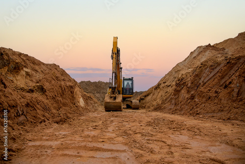 Excavator digs a large trench for pipe laying. Backhoe during earthmoving at construction site. Earth-moving heavy equipment