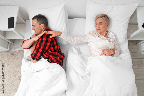 Offended mature couple lying after quarrel in bedroom