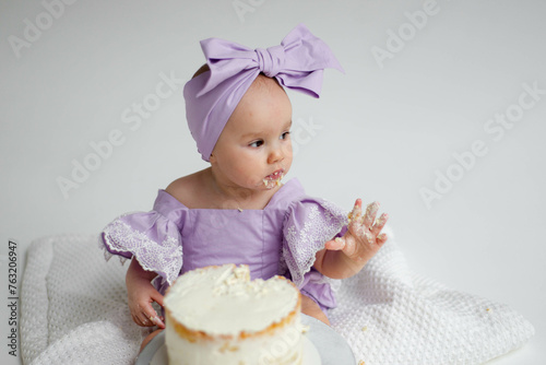 Cake crash. Photo session for baby's first birthday. Little elegant girl eats cake on a white background. Cyclorama.