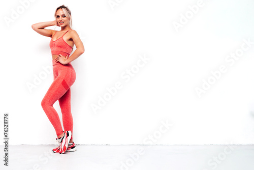 Fitness smiling woman in pink sports clothing. Young beautiful model with perfect body. Sexy female posing in studio near white wall. Doing exercises. Stretching out before training