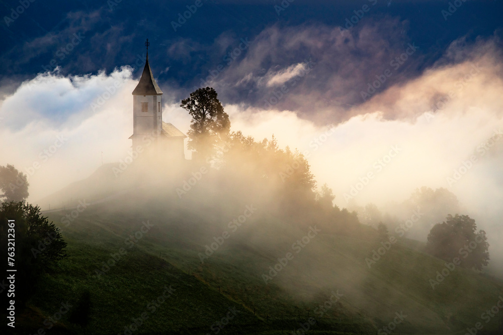 Fototapeta premium Jamnik, Slovenia - Magical foggy golden summer sunrise at Jamnik St.Primoz church.