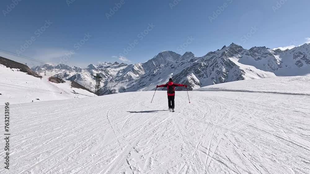 Skier skiing down on snow slope in mountain ski resort. Winter recreation. Raises hands side from freedom and feeling of flying. Positive emotions from speed of extreme sports with adrenaline in blood Skier skiing down on snow slope in mountain ski resort. Winter recreation. Raises hands side from freedom and feeling of flying. Positive emotions from speed of extreme sports with adrenaline in blood