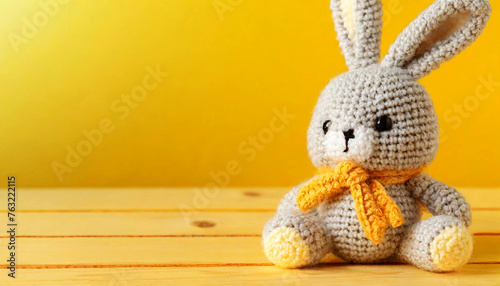 Closeup of a cute knitted easter bunny sitting on a wooden table against a yellow background with copy space. Template for an Easter greeting card. Generative Ai.